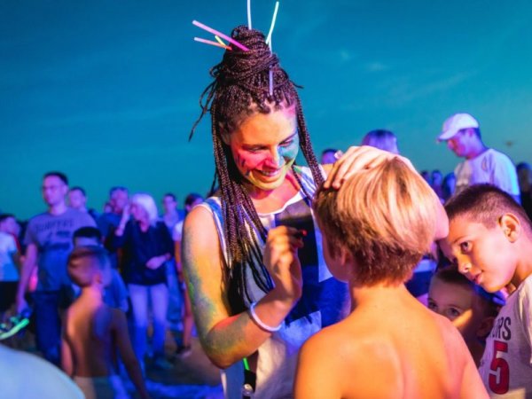 Una donna dipinge il viso di un bambino durante un evento serale all'aperto.