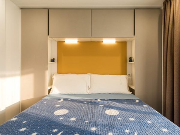 Letto matrimoniale con copriletto blu a tema spaziale, parete gialla e armadi grigi.