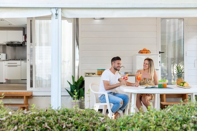 Coppia beve bevande a un tavolo all'aperto con piatti di frutta, davanti a una casa vacanze moderna.